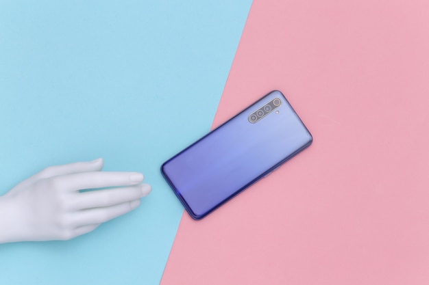 Manichino mano e smartphone su sfondo pastello blu-rosa. Arte di concetto di minimalismo. Vista dall'alto