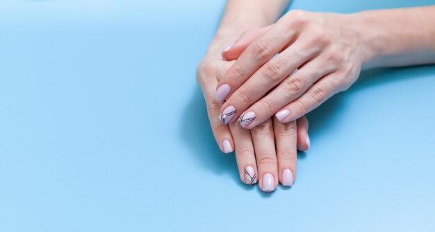 Manicure alla moda femminile alla moda. Le mani della bella giovane donna su fondo blu