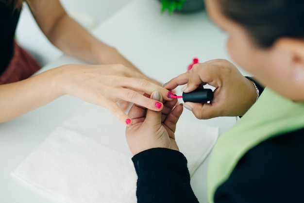 Manicure che applica smalto rosa alle unghie di una cliente in una spa o in un salone di bellezza