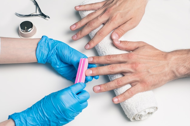 Manicure da uomo. Cosmetologo in guanti di gomma file unghie su mani maschili.