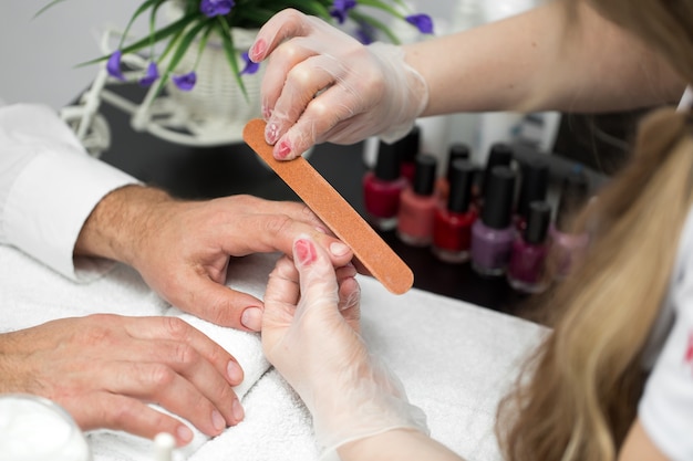 Manicure della ragazza che fa manicure per uomo nel salone di bellezza