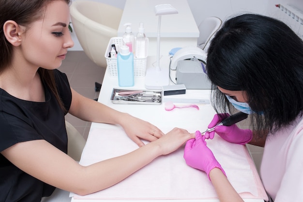 Manicure hardware nel moderno salone di bellezza. Estetista che fa la procedura di bellezza per il cliente, posto di lavoro professionale sullo sfondo