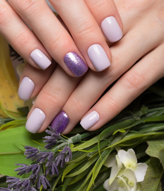 Manicure ordinata viola sulle mani femminili su uno sfondo di fiori. Disegno delle unghie