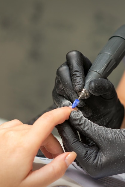 Manicure rimuove lo smalto per unghie utilizza la macchina elettrica della lima per unghie durante la manicure in un salone di bellezza.