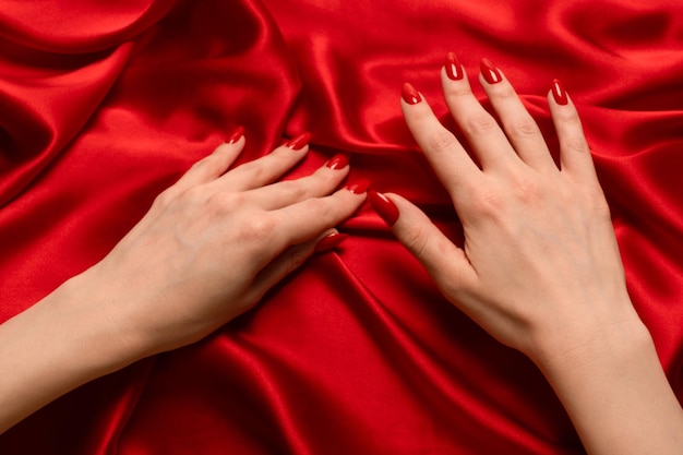 Manicure rossa sulle mani della donna su un backround di seta rossa di lusso