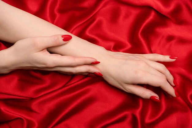 Manicure rossa sulle mani della donna su un backround di seta rossa di lusso