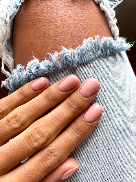 Mano abbronzata di una donna con una delicata manicure beige-rosa, che copre con smalto gel