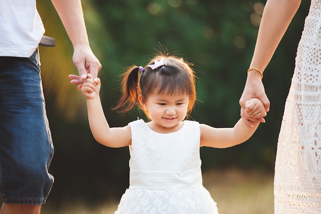 Mano asiatica sveglia della tenuta della bambina e camminare con i suoi genitori nel parco