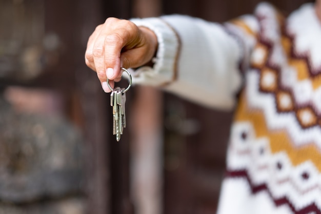 Mano caucasica della donna in maglione invernale che tiene le chiavi di casa davanti alla porta di legno. Affari, banche, concetto immobiliare