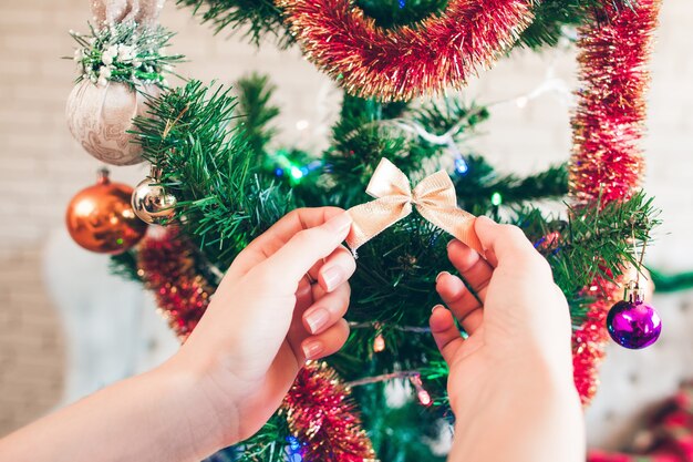 Mano che appende arco dorato sveglio sull'albero di Natale.