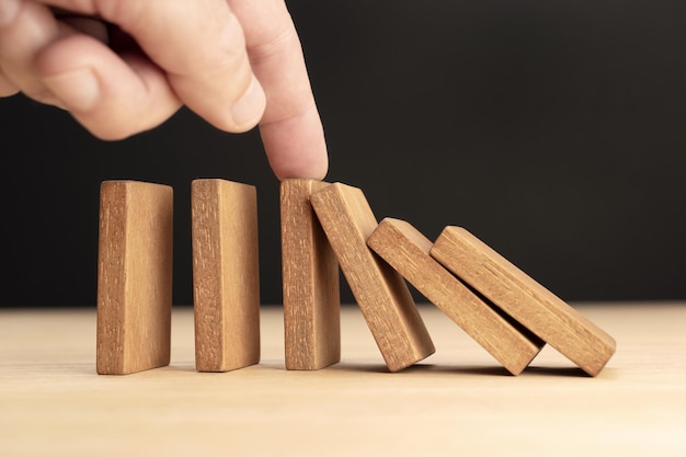 Mano che ferma l'effetto domino in legno che cade