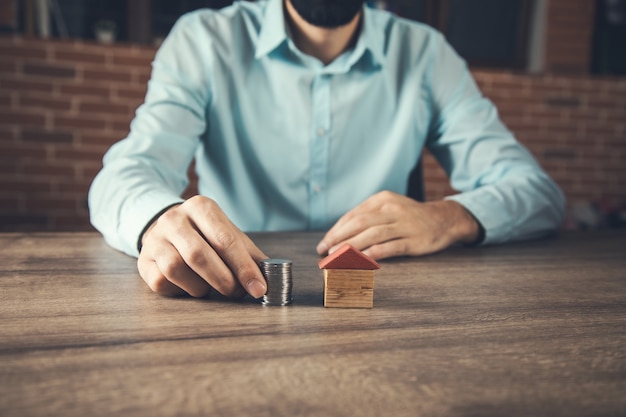 Mano che mette le monete sullo stack con il modello di casa. risparmiare denaro per l'acquisto di una casa