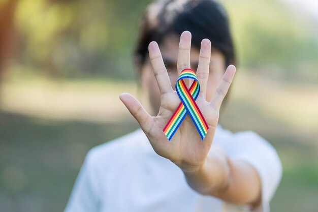 Mano che mostra il nastro arcobaleno LGBTQ contro il fondo del cielo al mattino.