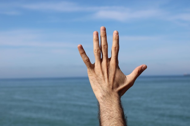 Mano che mostra il simbolo del gesto numero cinque sullo sfondo della natura del cielo estivo blu Numero 5