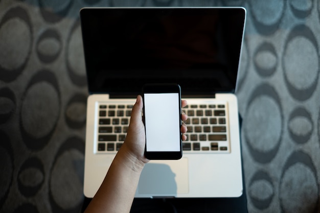 Mano che regge un telefono cellulare con schermo bianco bianco sul portatile