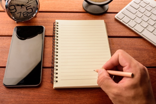 mano che scrive sul taccuino in bianco sulla tabella di legno con caffè, smartphone