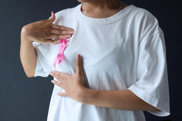 mano che tiene e spinge il seno e il nastro rosa di consapevolezza del cancro al seno sulla maglietta bianca femminile