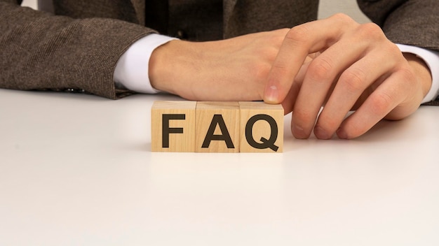 Mano che tiene i blocchi del cubo di legno con testo FAQ domande frequenti su sfondo bianco del tavolo concetti di marketing e business finanziari