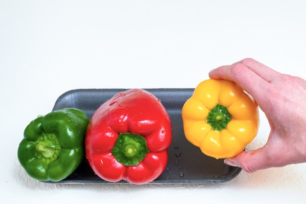 Mano che tiene i peperoni dolci gialli e per preparare insalata di peperoni gialli rossi e verdi, primo piano.