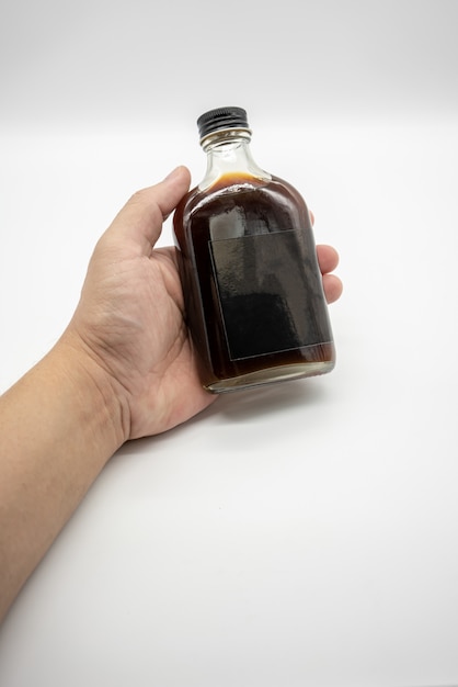 Mano che tiene il Cold Brew Coffee in bottiglia di vetro con tappo nero isolato su bianco