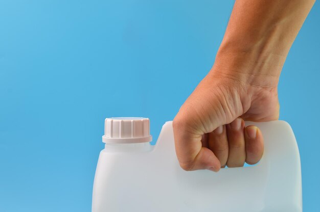 Mano che tiene il contenitore da gallone bianco isolato su uno sfondo blu