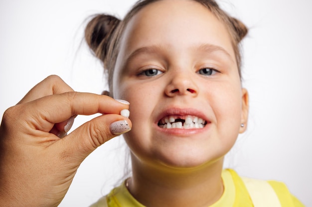 Mano che tiene il dente da latte strappato con la faccia della bambina che guarda l'obbiettivo e che mostra i denti dietro su...