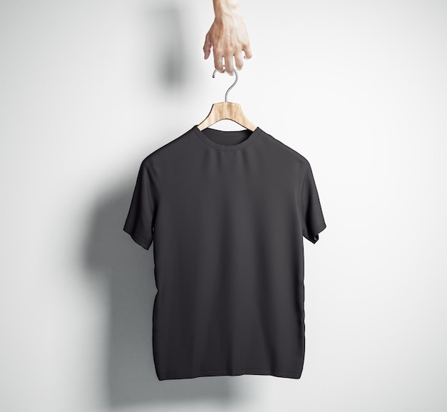 Mano che tiene il gancio con maglietta nera vuota su sfondo muro di cemento Design e concetto di negozio Mock up 3D Rendering