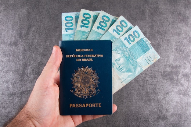 Mano che tiene il passaporto brasiliano con cento fatture reais.