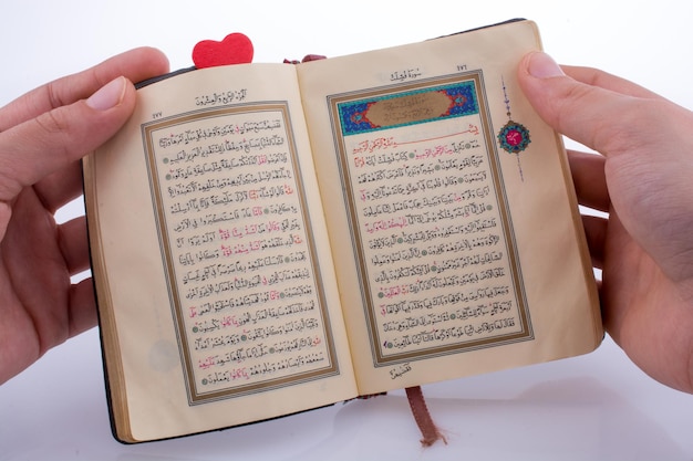Mano che tiene il Sacro Corano con un cuore su uno sfondo bianco