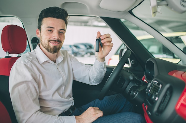 Mano che tiene il telecomando chiave auto, con sfondi di auto moderne. uomo seduto all'interno della nuova auto con le chiavi.