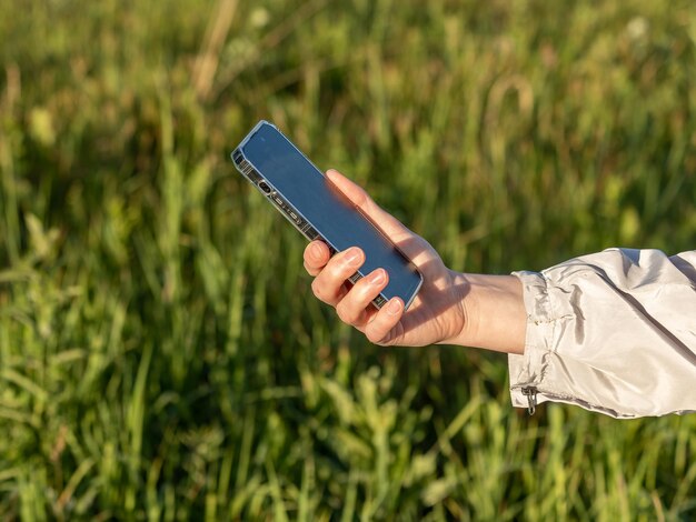 Mano che tiene il telefono cellulare sopra la natura dell'erba verde