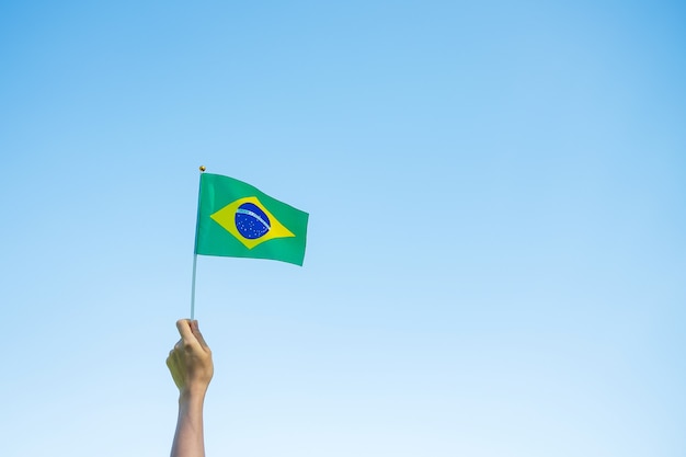 Mano che tiene la bandiera del Brasile sul fondo del cielo blu. Concetti di festa dell'indipendenza di settembre e felice celebrazione