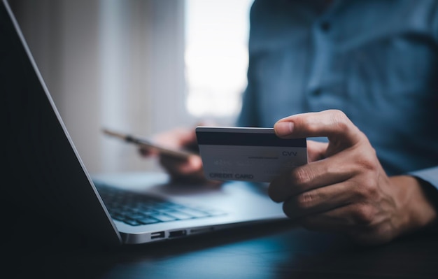 Mano che tiene la carta di credito per effettuare un acquisto su Internet sul computer portatile con carta di credito pagamento online shopping online e-commerce internet banking spesa denaro concetto