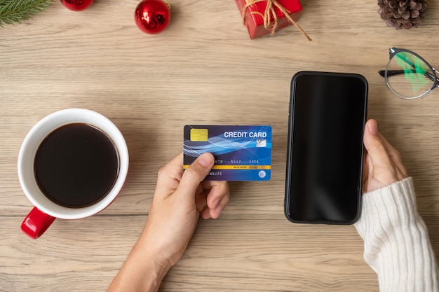 Mano che tiene la carta di credito per lo shopping online sullo smartphone durante il consumo di caffè Buon Natale alla vigilia di dicembre, vendita stagionale del Black Friday, Capodanno e concetto di vacanza