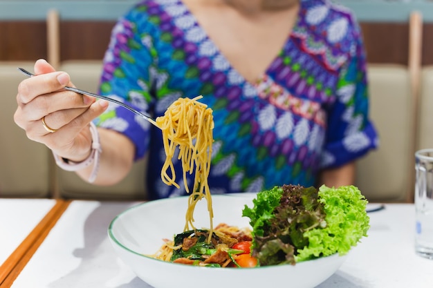 Mano che tiene la forchetta che mangia gli spaghetti nel ristorante