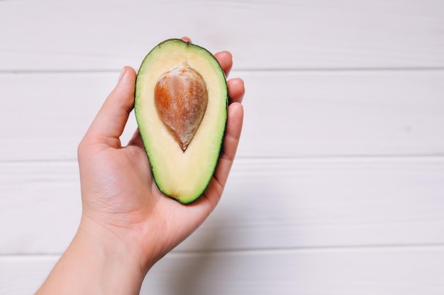 Mano che tiene la metà di avocado su sfondo bianco cibo sano