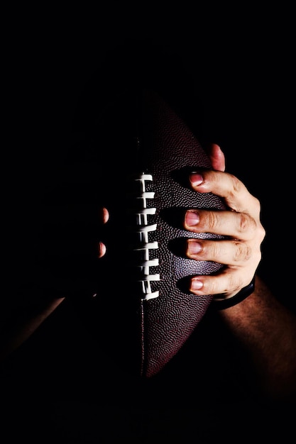 Mano che tiene la palla da football americano isolata su sfondo nero