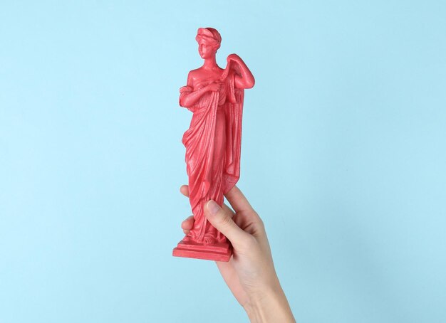 Mano che tiene la statua antica rosa su sfondo blu