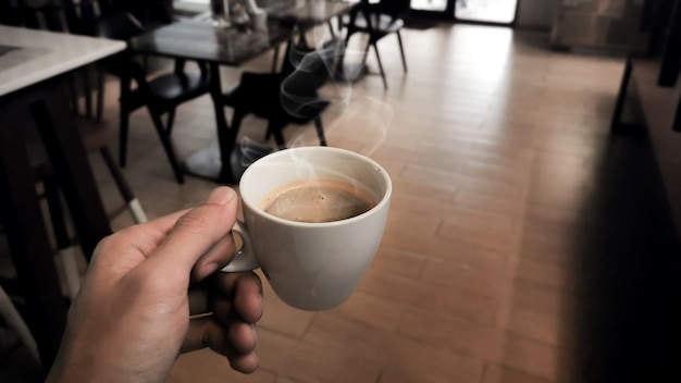 Mano che tiene la tazza bianca di caffè caldo