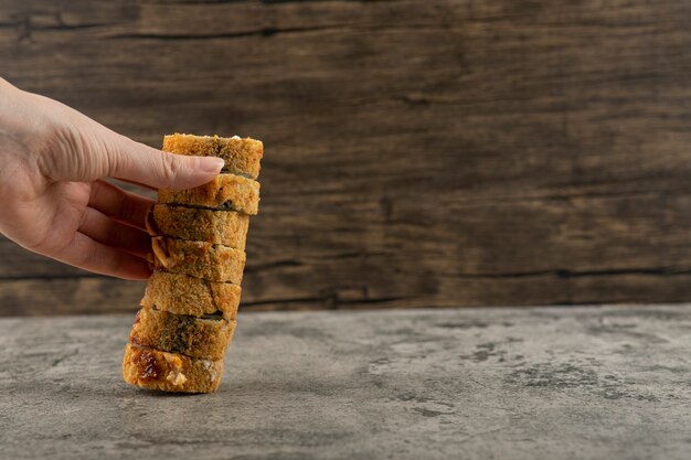 Mano che tiene la torre di rotoli di sushi tempura sul tavolo di pietra.