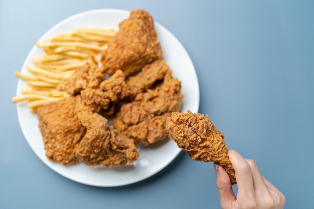 Mano che tiene le bacchette, pollo fritto croccante con patatine fritte nel piatto bianco su sfondo blu.