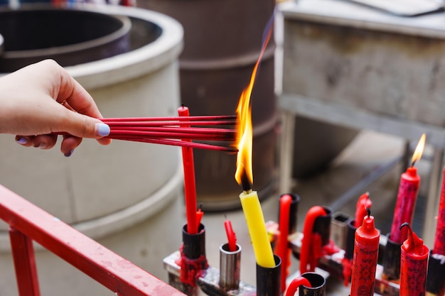 Mano che tiene per accendere l'incenso rosso con la fiamma della candela nel tempio