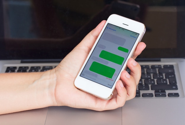 Mano che tiene smartphone con nuvole sms vuote su sfondo laptop