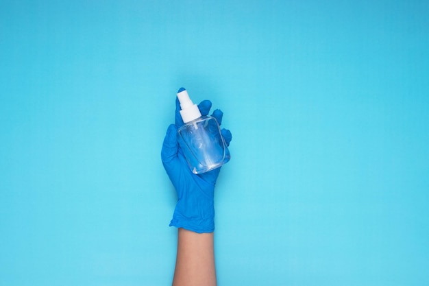 Mano che tiene spray disinfettante con guanti medici blu su sfondo azzurro