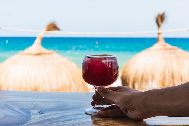 Mano che tiene un bicchiere di vino davanti alla spiaggia