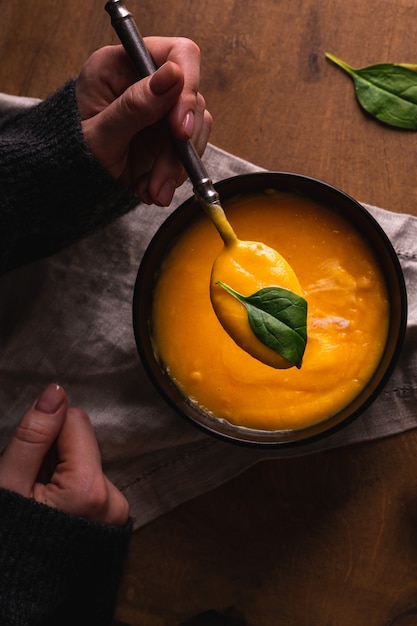 Mano che tiene un cucchiaio con zuppa di zucca