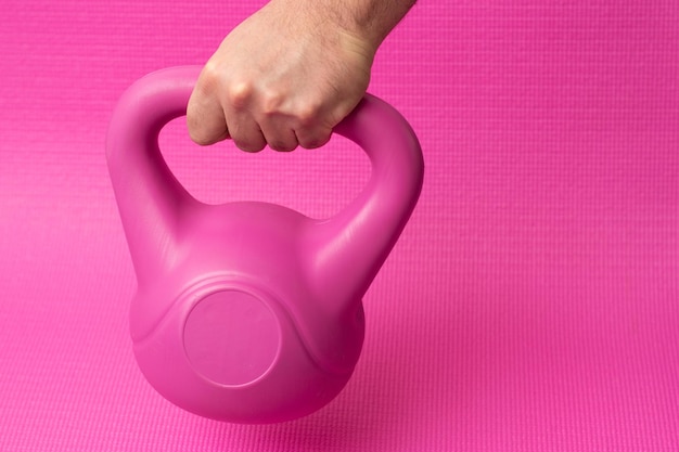 Mano che tiene un kettlebell rosa che esce dall'alto con sfondo rosa e spazio per la copia