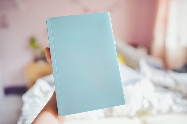 Mano che tiene un libro blu con una copertina vuota, c'è spazio per il testo in camera da letto.
