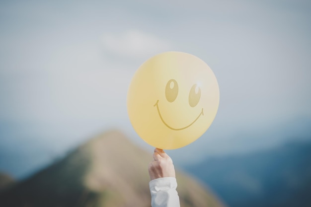 Mano che tiene un palloncino giallo con una faccia sorridente luminosa