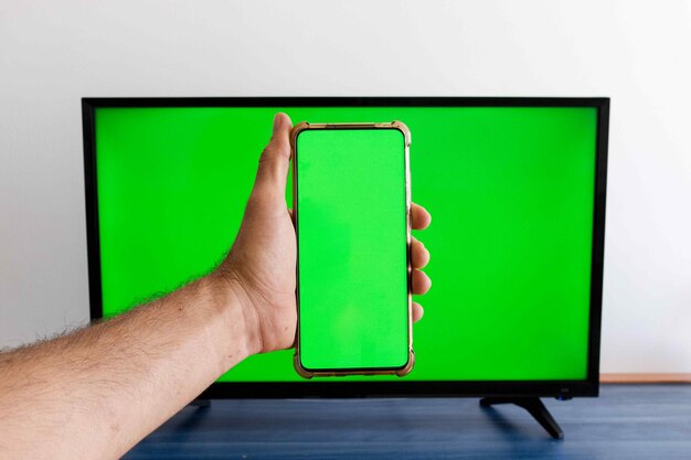 Mano che tiene un telefono cellulare con schermo verde con un televisore a schermo verde sullo sfondo